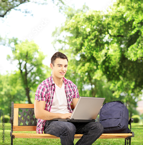 Photo: Smiling male student sitting on a bench and working on a laptop Smiling male student sitting on a bench and working on a laptop