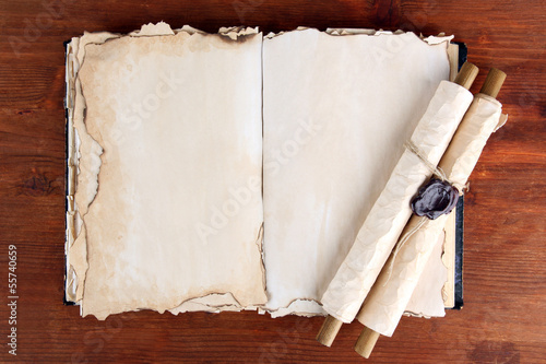 Photo: Open old book and scrolls on wooden background Open old book and scrolls on wooden background