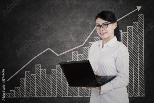 Photo: Attractive female holding laptop on profit bar chart Attractive female holding laptop on profit bar chart