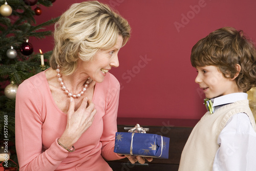 Photo: Junge überreicht Weihnachtsgeschenk an Großmutter, lächelnd Junge überreicht Weihnachtsgeschenk an Großmutter, lächelnd