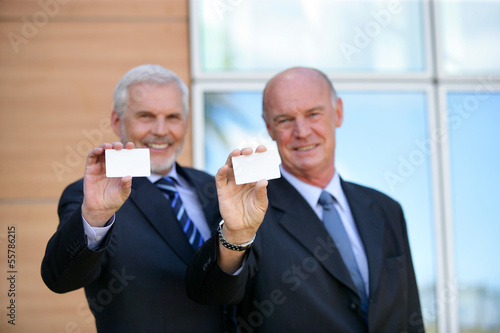 Photo: Two senior businessmen showing cards Two senior businessmen showing cards