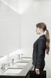 Photo: Young businesswoman with long hair looking into the mirror and preparing herself in the bathroom Young businesswoman with long hair looking into the mirror and preparing herself in the bathroom