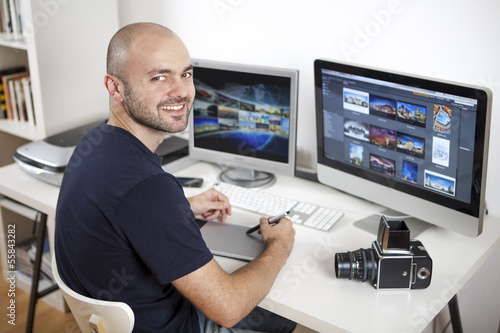 Photo: Jeune homme photographe retouchant ses photos sur son ordinateur Jeune homme photographe retouchant ses photos sur son ordinateur