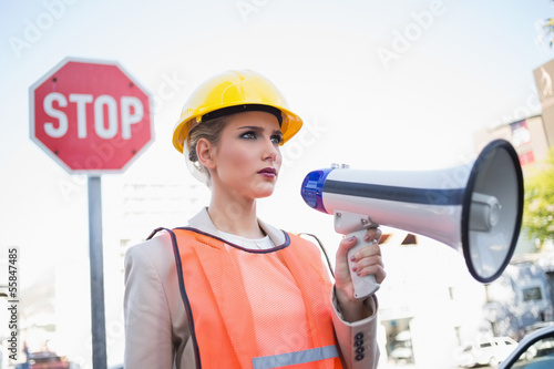 Photo: Frowning businesswoman wearing builders clothes holding megaphon Frowning businesswoman wearing builders clothes holding megaphon