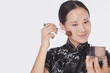 Photo: Woman in traditional clothing looking into a mirror and applying make up with a make up brush, studio shot Woman in traditional clothing looking into a mirror and applying make up with a make up brush, studio shot