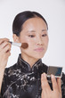 Photo: Woman in traditional clothing looking into a mirror and applying make up with a make up brush, studio shot Woman in traditional clothing looking into a mirror and applying make up with a make up brush, studio shot