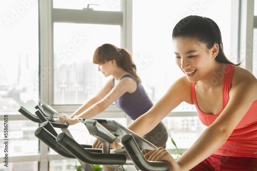 Photo: Young women on stationary bikes exercising in the gym Young women on stationary bikes exercising in the gym