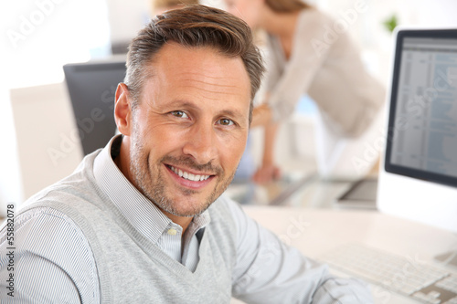 Photo: Cheerful man sitting in office and working on desktop Cheerful man sitting in office and working on desktop