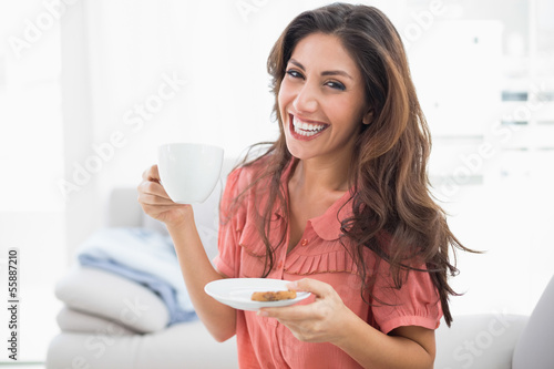 Photo: Happy brunette sitting on her sofa holding cup and saucer Happy brunette sitting on her sofa holding cup and saucer