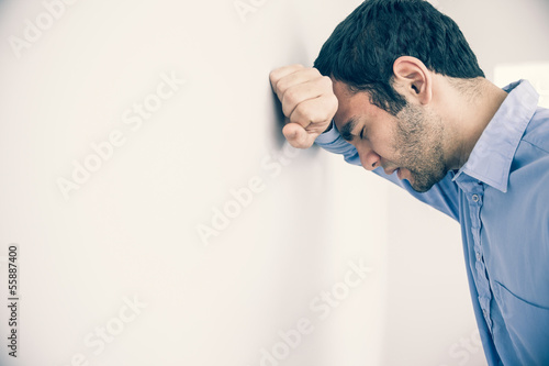 Photo: Depressed man leaning his head against a wall Depressed man leaning his head against a wall