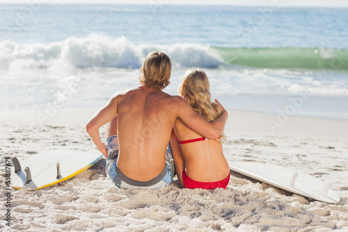Photo: Rear view of a couple sitting on the beach and looking at the se Rear view of a couple sitting on the beach and looking at the se