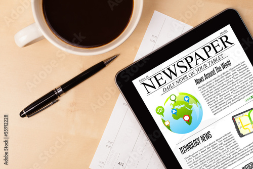 Photo: Tablet pc shows news on screen with a cup of coffee on a desk Tablet pc shows news on screen with a cup of coffee on a desk