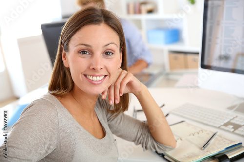 Photo: Young businesswoman sitting at desk in office Young businesswoman sitting at desk in office
