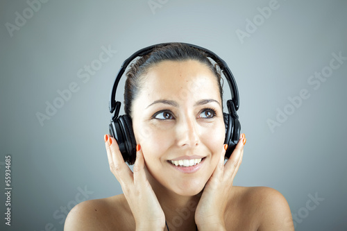 Photo: Portrait of a young woman with headphones listening music over g Portrait of a young woman with headphones listening music over g