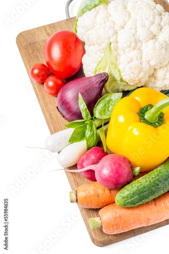 Photo: Fresh vegetables at wood cutting board isolated on white Fresh vegetables at wood cutting board isolated on white