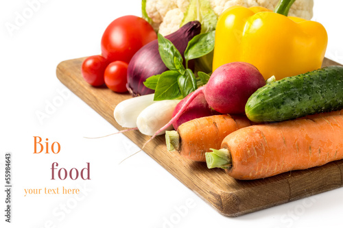 Photo: Fresh vegetables at wood cutting board isolated on white Fresh vegetables at wood cutting board isolated on white