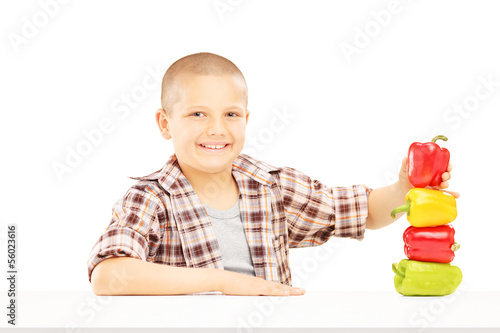 Photo: Little smiling boy holding colorful peppers on a table Little smiling boy holding colorful peppers on a table