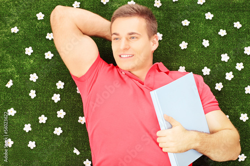 Photo: Young male with book lying on a grass with daisies Young male with book lying on a grass with daisies