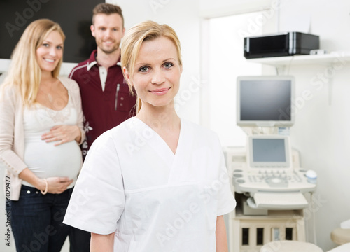 Photo: Confident Doctor With Expectant Couple In Background Confident Doctor With Expectant Couple In Background