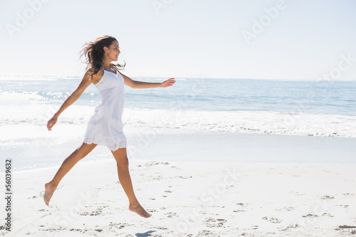 Photo: Happy brunette in white sun dress skipping on the sand Happy brunette in white sun dress skipping on the sand