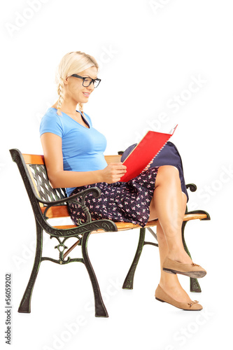 Photo: Smiling blond female student sitting on a bench reading a book Smiling blond female student sitting on a bench reading a book
