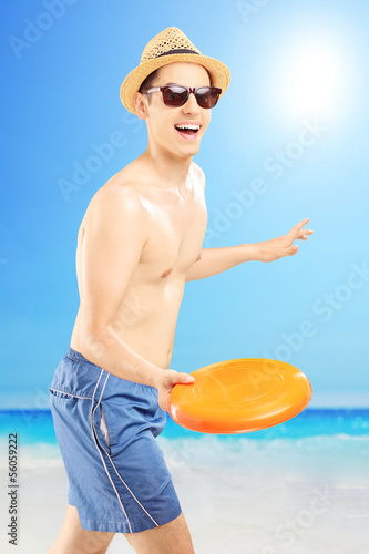 Photo: Smiling guy in swimming shorts throwing frizbee, on a beach Smiling guy in swimming shorts throwing frizbee, on a beach
