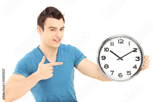 Photo: Young smiling male pointing with his hand on a wall clock Young smiling male pointing with his hand on a wall clock