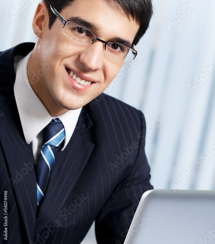 Photo: Smiling businessman working with laptop at office Smiling businessman working with laptop at office