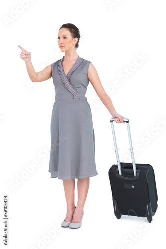 Photo: Smiling gorgeous woman carrying her suitcase pointing finger Smiling gorgeous woman carrying her suitcase pointing finger