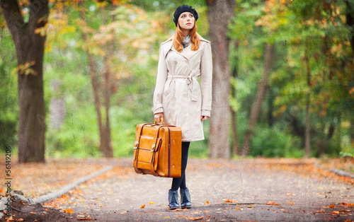 Photo: Redhead girl with suitcase at autumn outdoor. Redhead girl with suitcase at autumn outdoor.