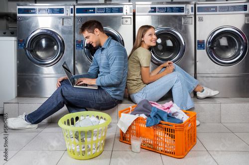 Photo: Couple Using Laptop And Earphones At Laundry Couple Using Laptop And Earphones At Laundry