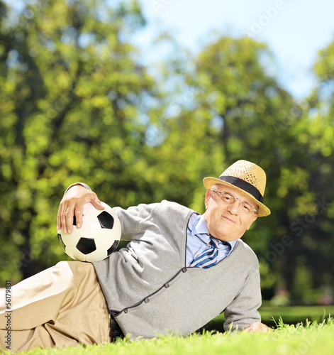 Photo: Senior man with hat lying on a grass and holding a soccer ball Senior man with hat lying on a grass and holding a soccer ball