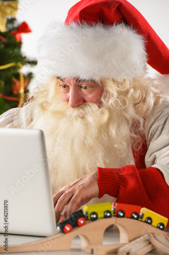 Photo: Real Santa Claus working on laptop with surprised face at home Real Santa Claus working on laptop with surprised face at home