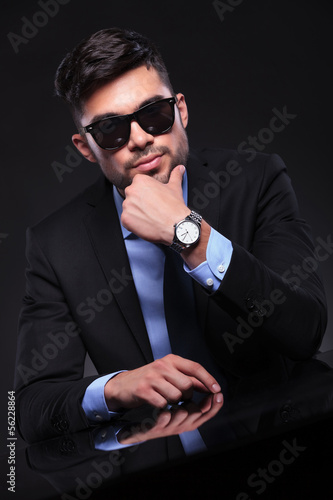 Photo: young business man stands with hand on chin at desk young business man stands with hand on chin at desk