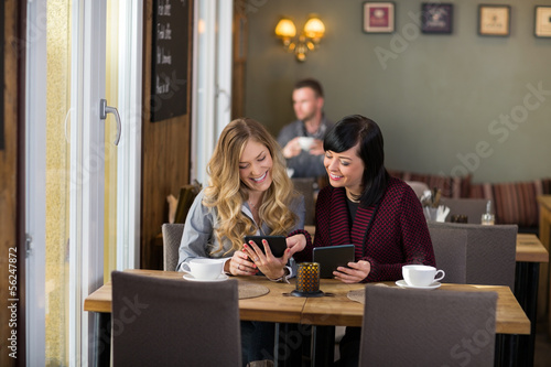 Photo: Female Friends Using Digital Tablets At Table Female Friends Using Digital Tablets At Table