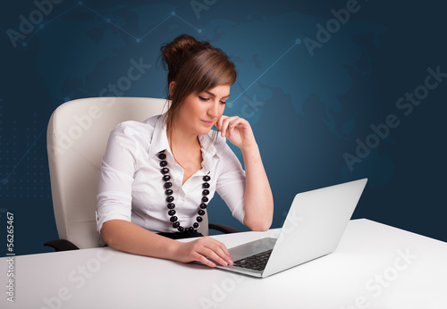 Photo: Young woman sitting at desk and typing on laptop Young woman sitting at desk and typing on laptop