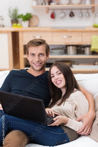 Photo: junges lächelndes paar sitzt mit laptop auf dem sofa junges lächelndes paar sitzt mit laptop auf dem sofa