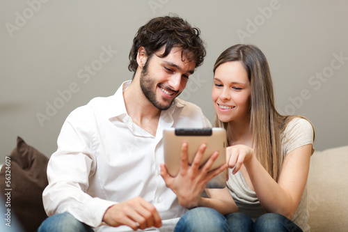 Photo: In love couple using a tablet computer in their living room In love couple using a tablet computer in their living room