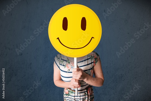 Photo: Young woman holding a smiley face emoticon Young woman holding a smiley face emoticon
