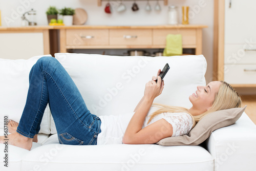 Photo: junge frau liegt auf dem sofa und schaut auf ihr handy junge frau liegt auf dem sofa und schaut auf ihr handy