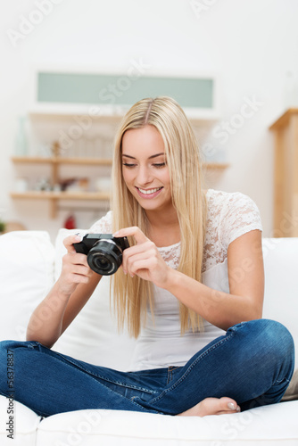 Photo: junge frau sitzt auf dem sofa und schaut auf ihre digitalkamera junge frau sitzt auf dem sofa und schaut auf ihre digitalkamera