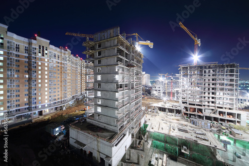 Photo: Lit high multi-storey buildings under construction and cranes Lit high multi-storey buildings under construction and cranes