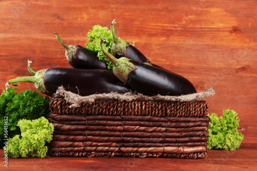 Photo: Fresh eggplants in wicker basket on table on wooden background Fresh eggplants in wicker basket on table on wooden background