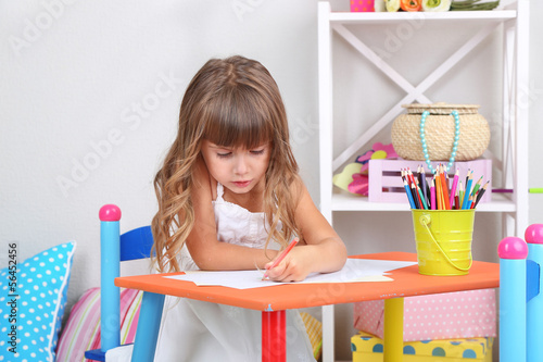 Photo: Little girl draws sitting at table in room Little girl draws sitting at table in room