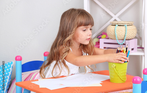 Photo: Little girl draws sitting at table in room Little girl draws sitting at table in room