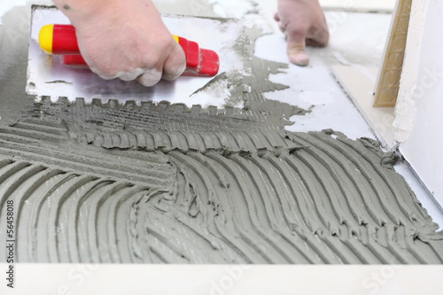 Photo: Construction worker is tiling at home, tile floor adhesive Construction worker is tiling at home, tile floor adhesive