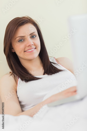 Photo: Content girl looking at camera and using a laptop lying on a bed Content girl looking at camera and using a laptop lying on a bed