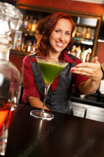 Photo: Cheerful barmaid with cocktail behind bar counter Cheerful barmaid with cocktail behind bar counter