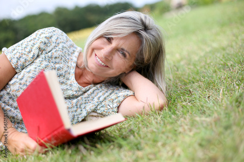 Photo: Senior woman reading book laid on the grass Senior woman reading book laid on the grass