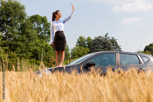 Photo: Businesswoman searching phone signal while standing on her car Businesswoman searching phone signal while standing on her car